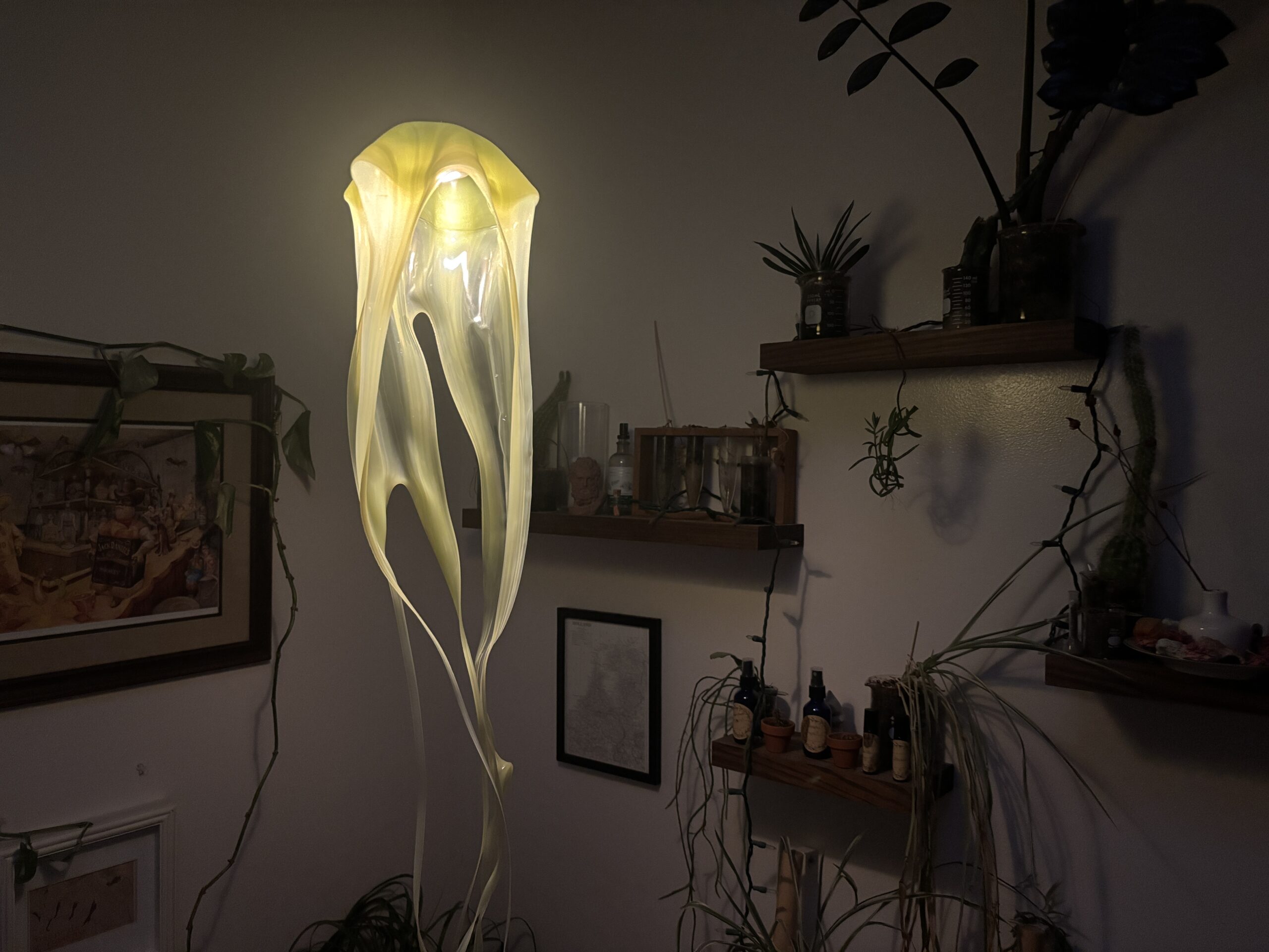 Pale yellow jellyfish hanging lamp glowing in a dim room with wall shelves and plants