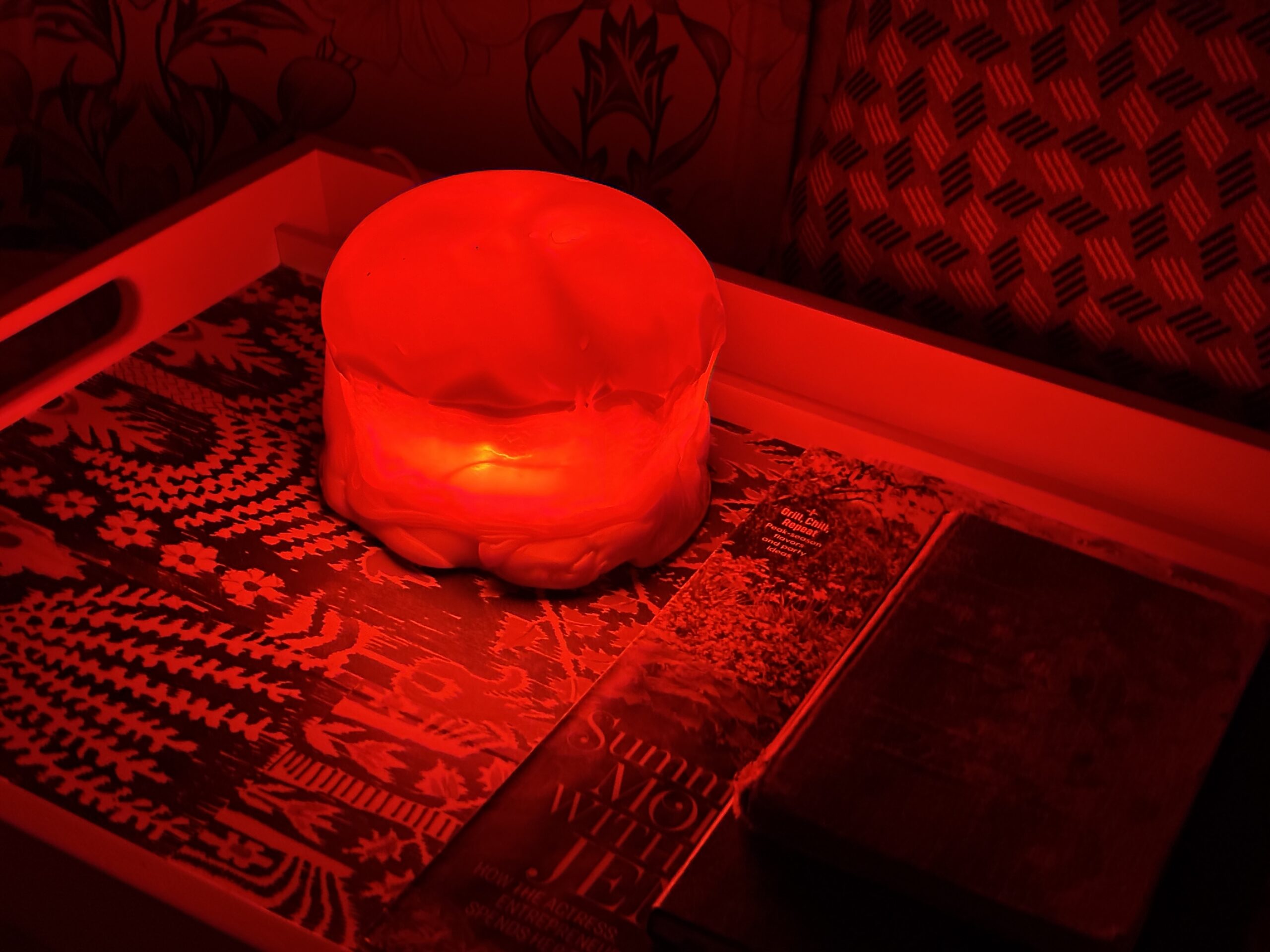 Red jellyfish dome lamp glowing on a tray beside magazines in a red-lit room