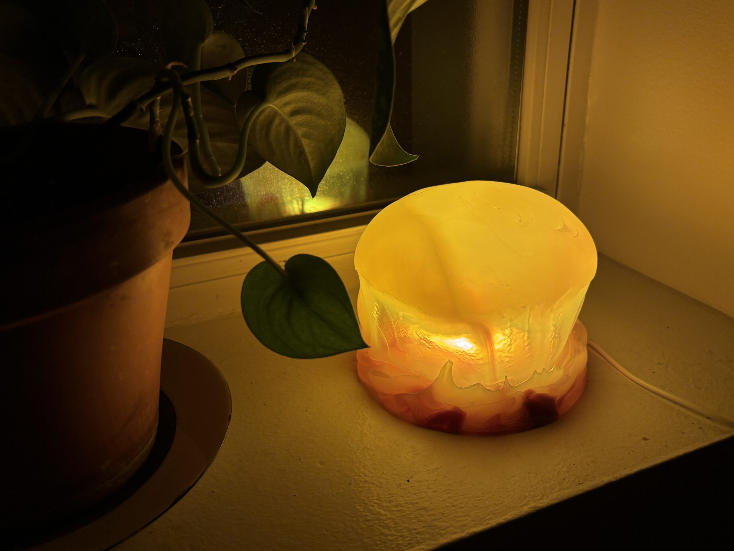 Amber jellyfish dome lamp glowing on a windowsill beside a trailing houseplant