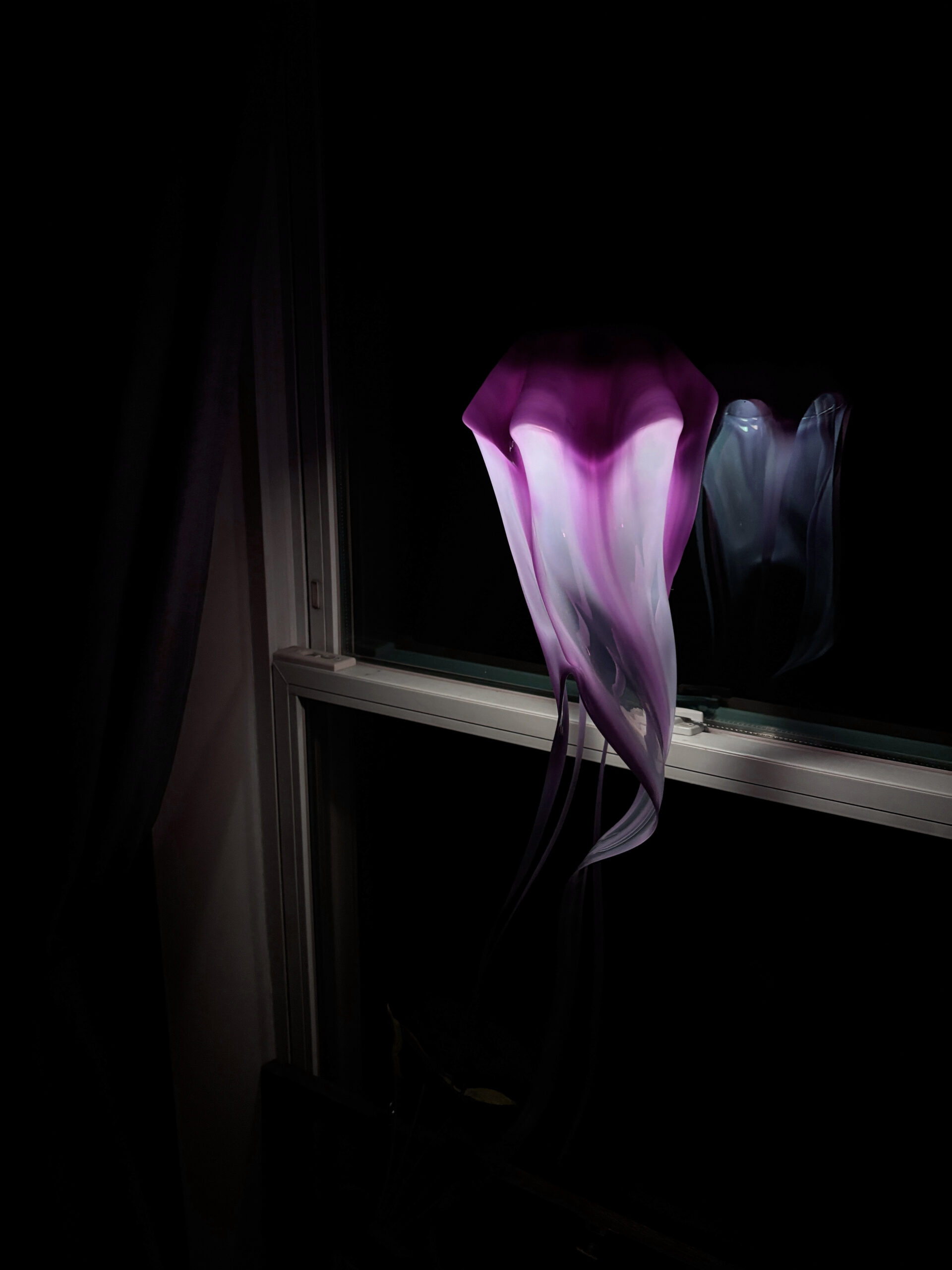 Light purple jellyfish hanging lamp glowing in front of a window at night