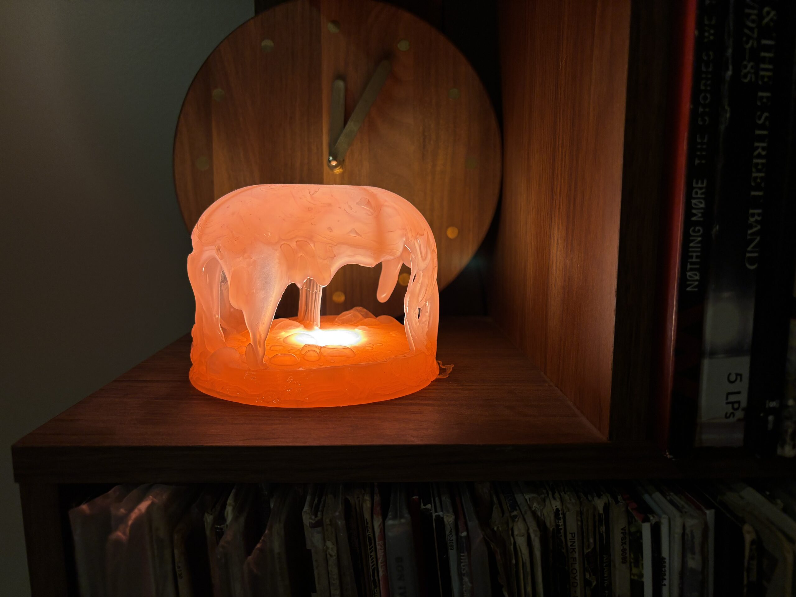 Orange jellyfish dome lamp with an open cave-like base glowing on a shelf of vinyl records