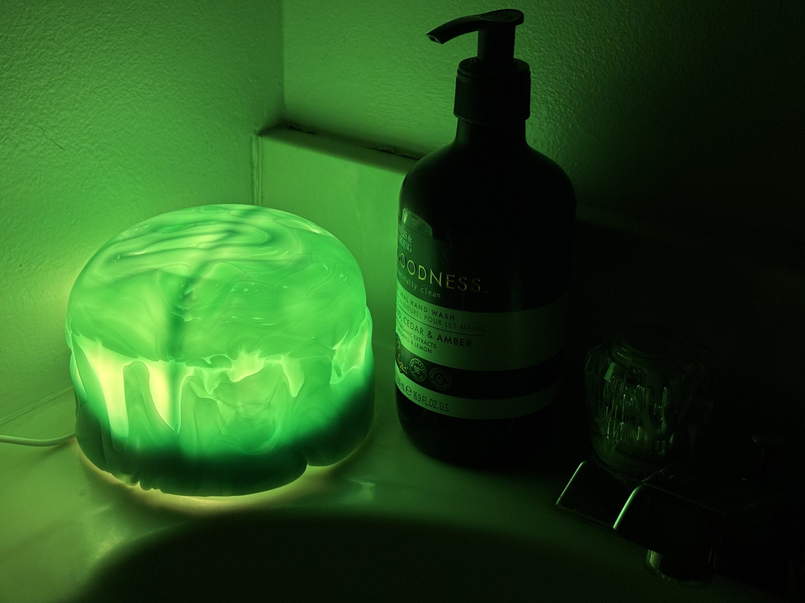 Green jellyfish dome lamp glowing on a bathroom counter beside a hand soap bottle