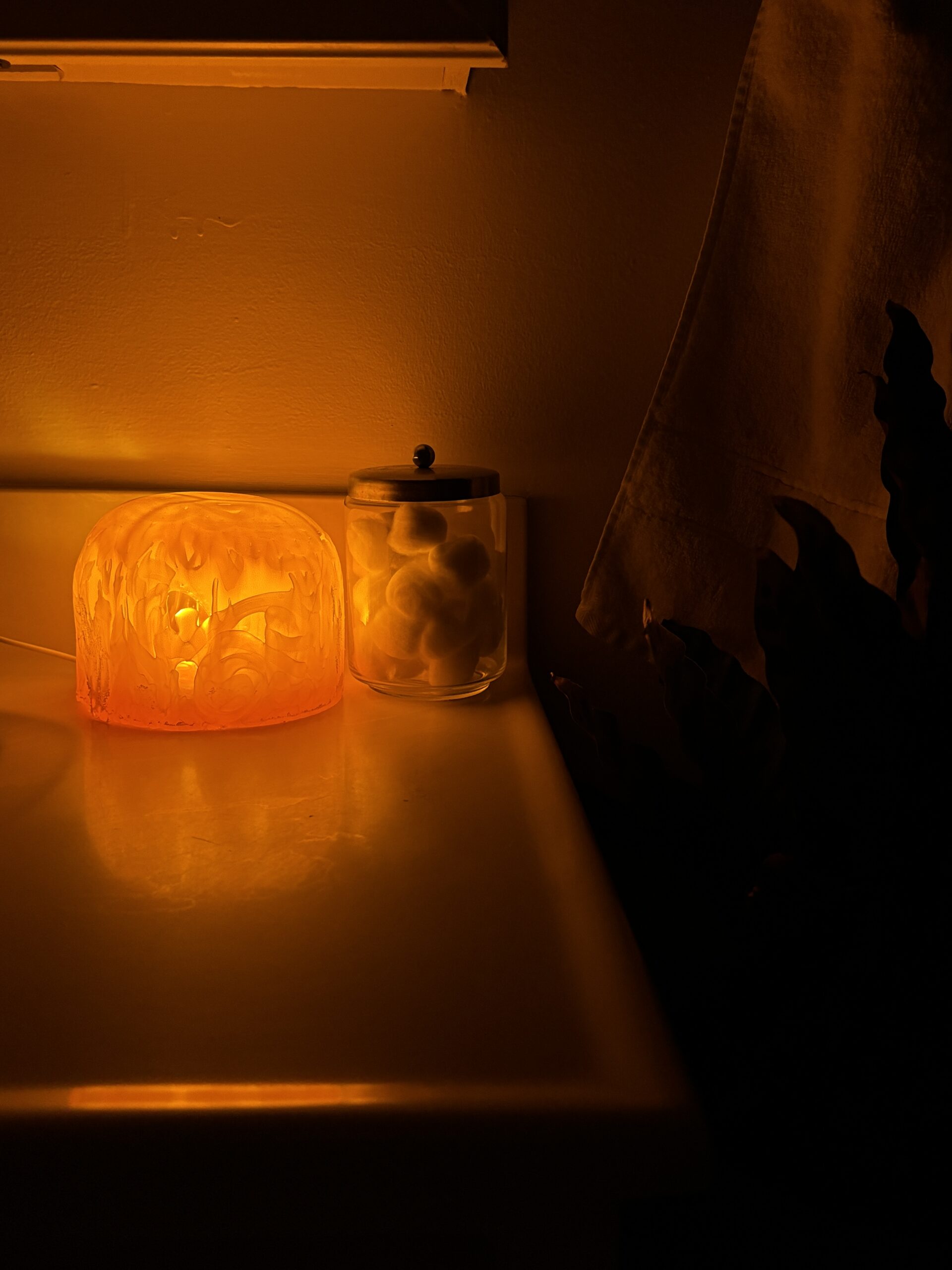 Amber jellyfish dome lamp with a textured swirl surface glowing beside a jar of cotton balls