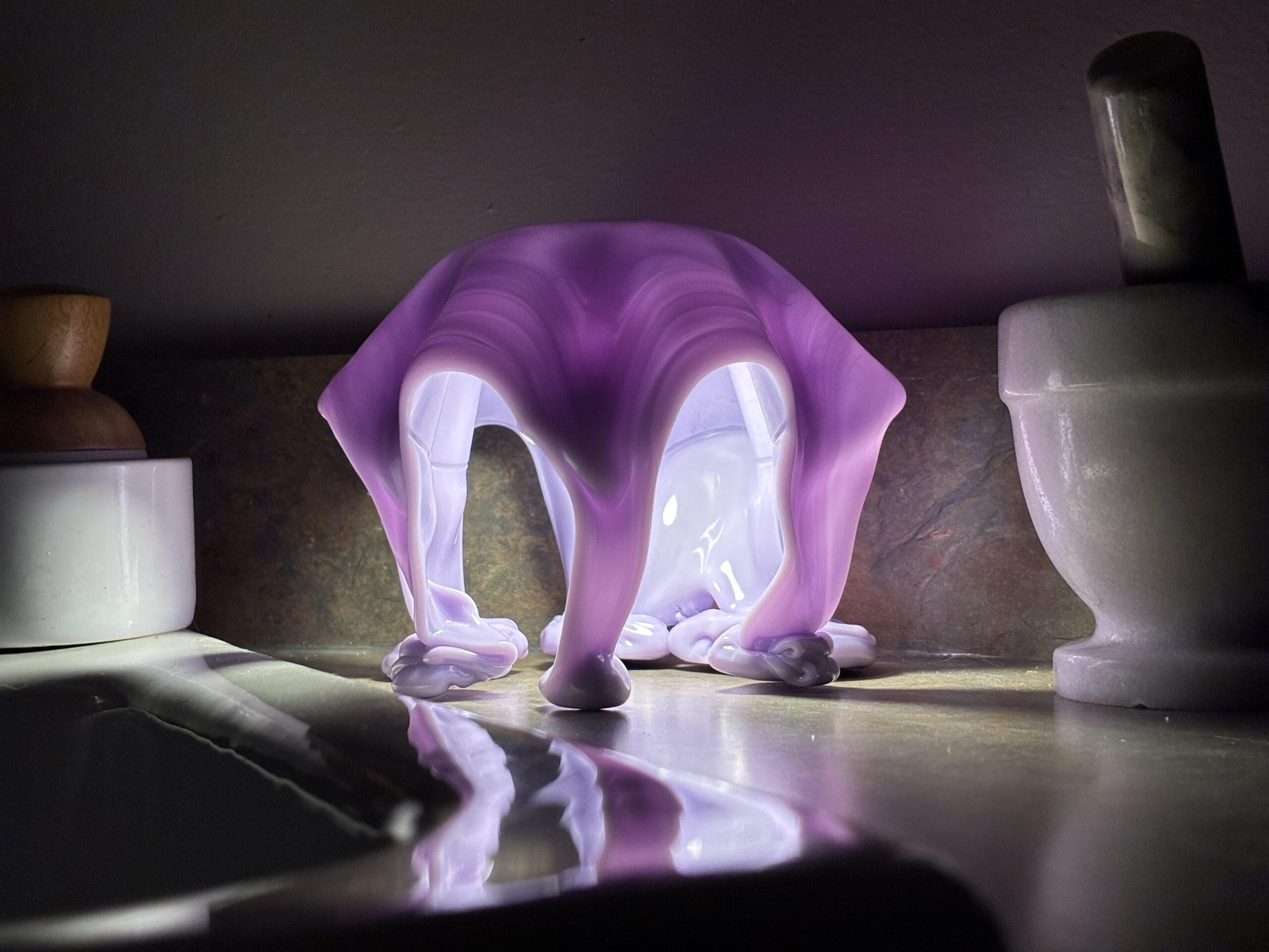 Lavender jellyfish table lamp glowing on a bathroom counter beside stone accessories